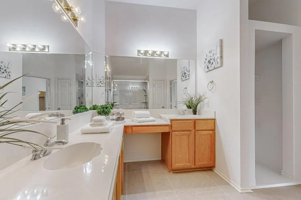Bathroom featuring dual undermount sinks, an extended vanity with wood-finish cabinetry, a dedicated vanity seating area, a large wall-mounted mirror, and tile flooring