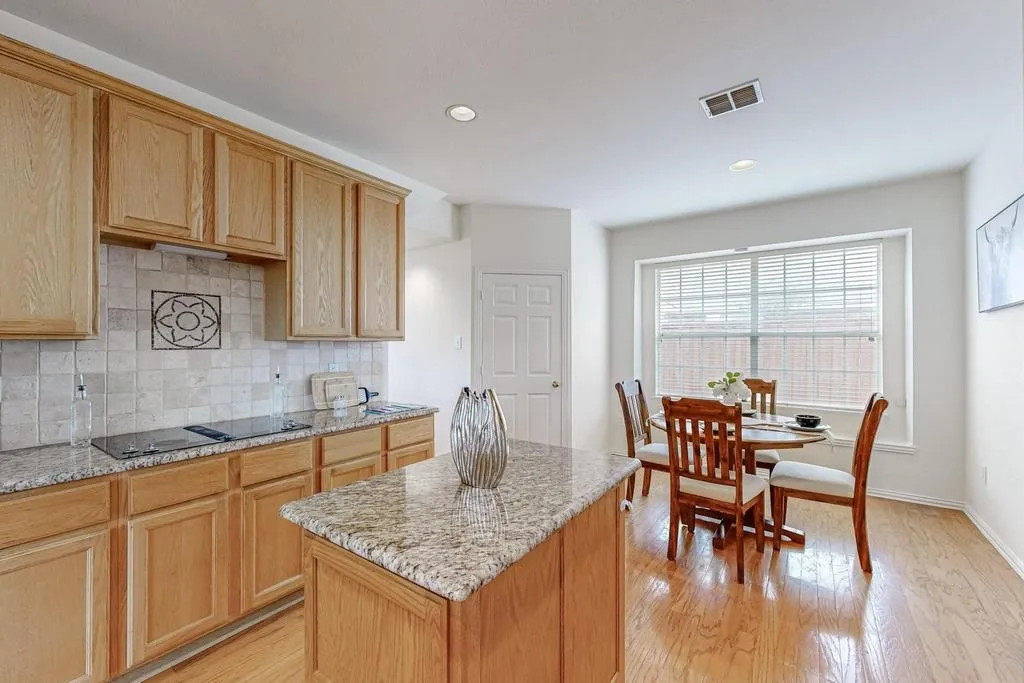 Kitchen featuring wood-finish cabinetry, speckled granite countertops, a tiled backsplash with decorative inlay, and a built-in cooktop