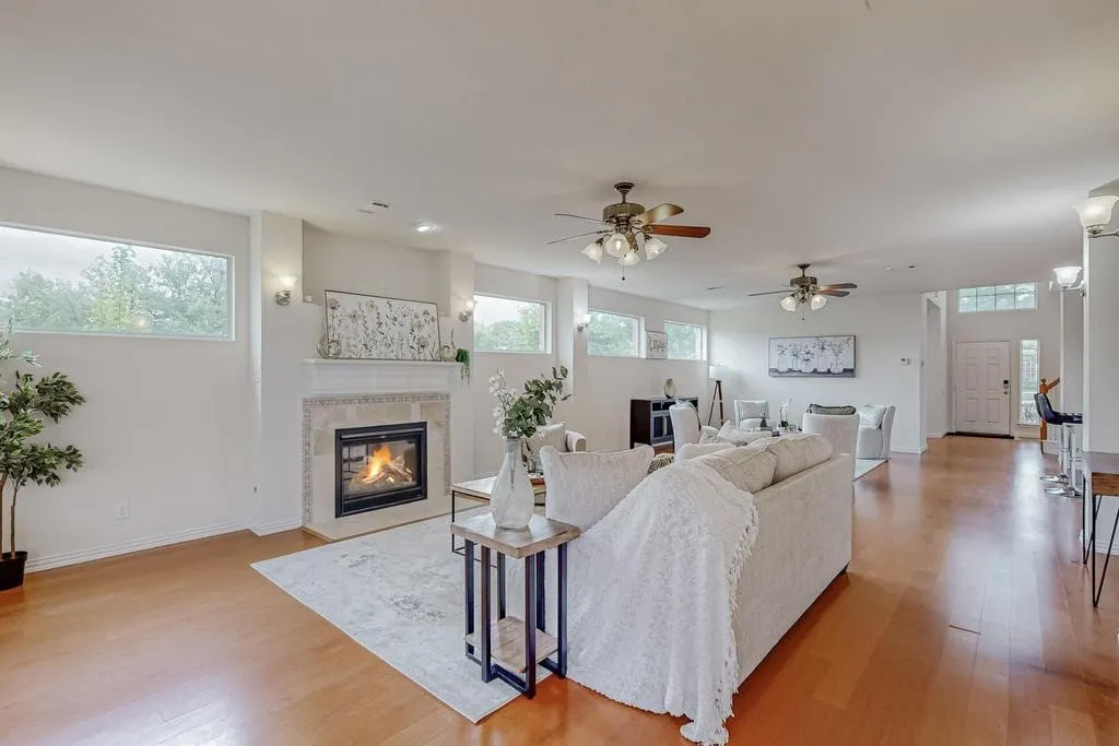 Living area featuring wood-finish flooring, a fireplace with a stone surround and mantel, multiple windows, and two ceiling fans