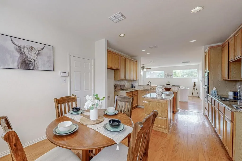 Open-concept kitchen featuring light wood cabinetry, granite countertops, wood-finish flooring, a kitchen island with additional storage, and recessed lighting