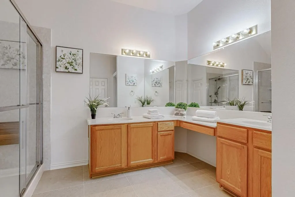 Dual vanity with light wood cabinetry and white countertops, featuring ample storage, integrated sinks, and separate mirrors with vanity lighting