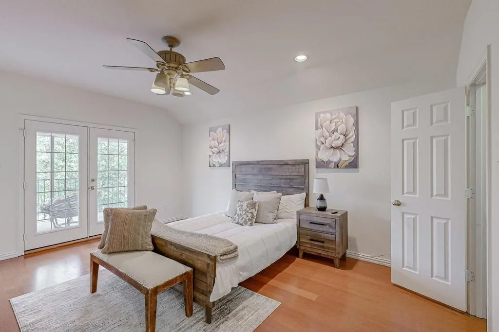 Bright room featuring warm wood-finish flooring, a ceiling fan with integrated lighting, and a white six-panel interior door