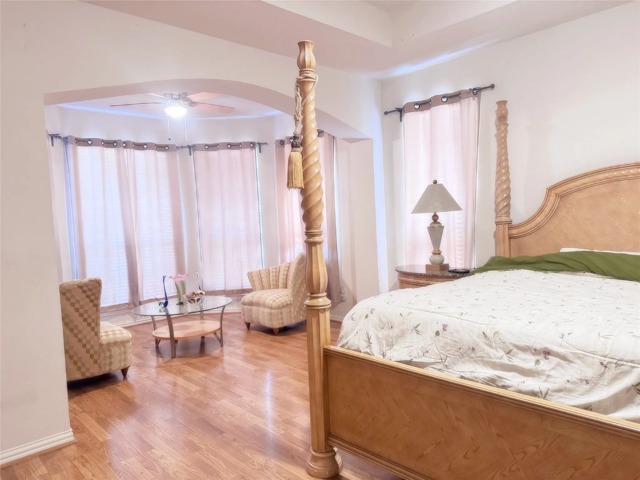 Spacious room featuring wood-finish flooring, a tray ceiling, and an arched entryway leading to a bay window alcove