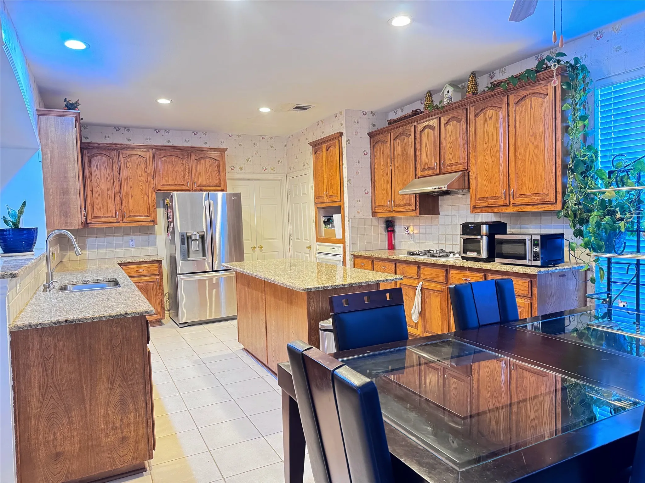 Spacious kitchen featuring extensive wood cabinetry, granite countertops, tile flooring, a stainless steel refrigerator, and a kitchen island with seating