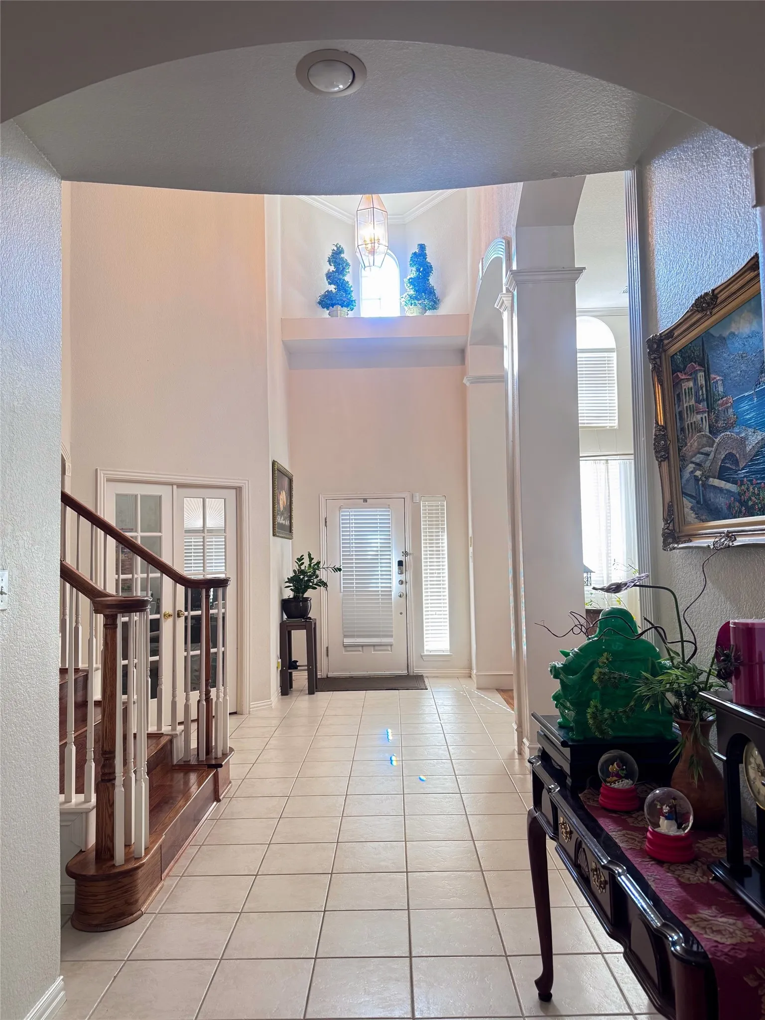 Two-story foyer featuring tile flooring, a prominent wooden staircase with white balusters, and a front entry door with vertical glass inserts