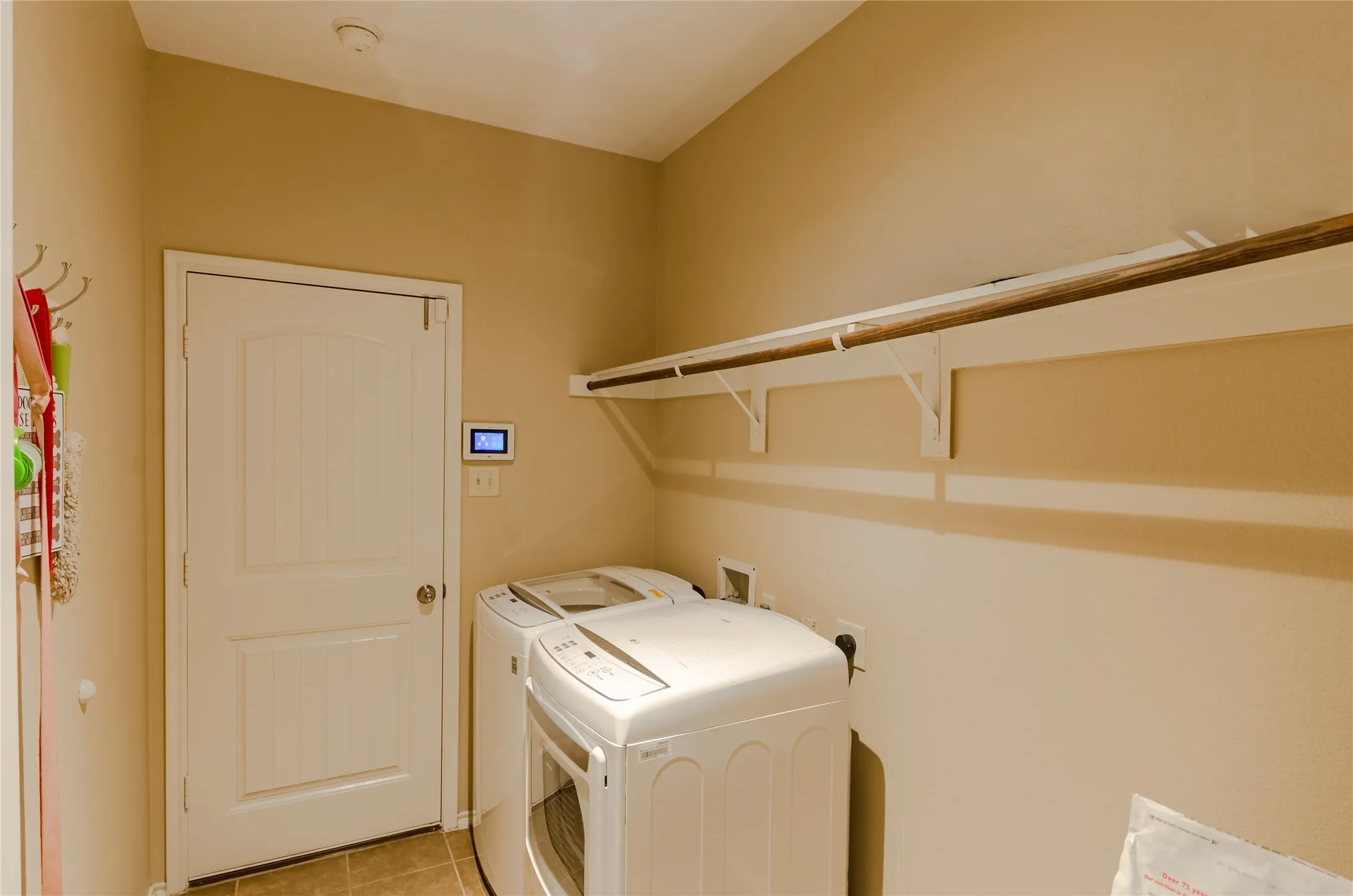 Utility area featuring a paneled door, wall-mounted shelving with a hanging rod, and tile flooring