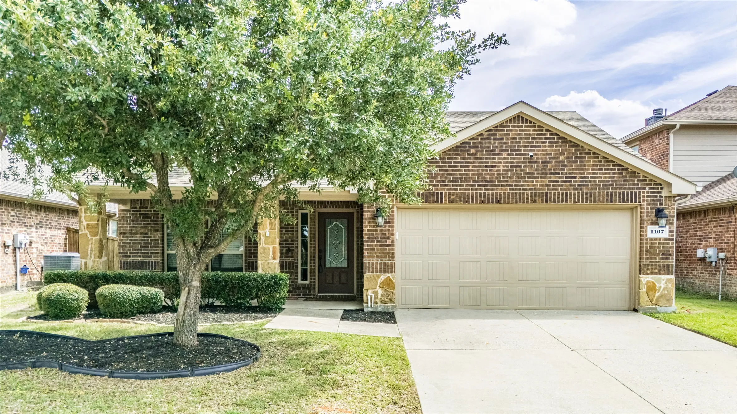 Brick exterior featuring stone accents, a covered front entry, and an attached two-car garage