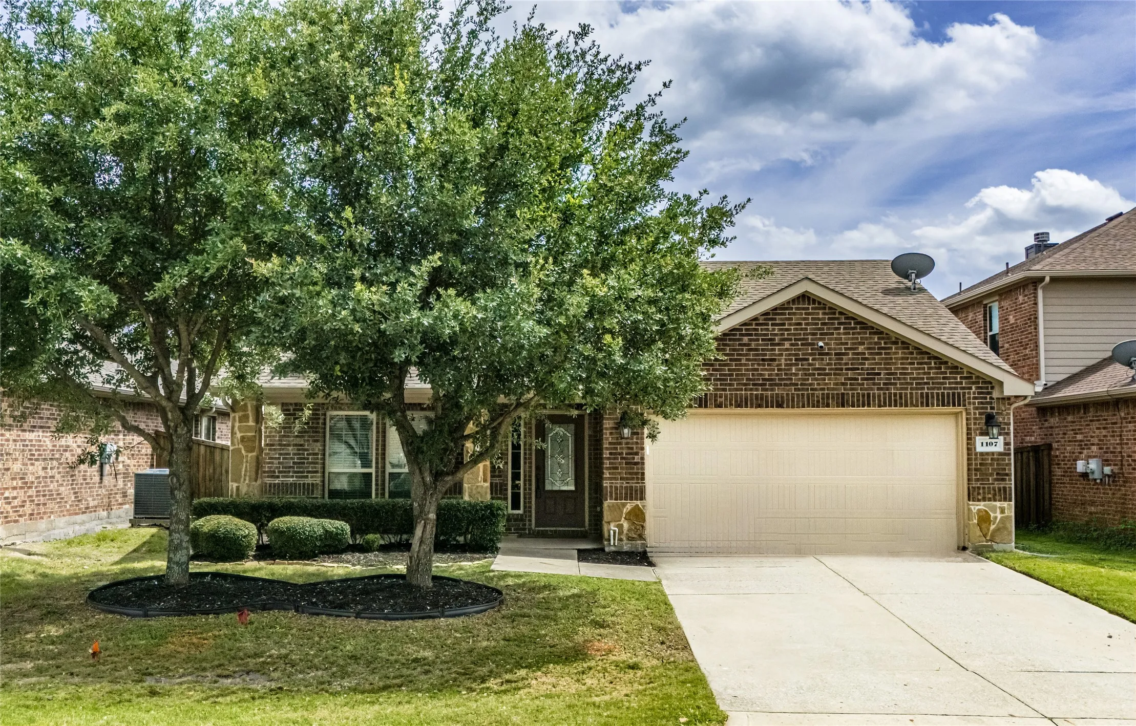 Brick facade residence featuring a two-car garage, concrete driveway, and mature landscaping