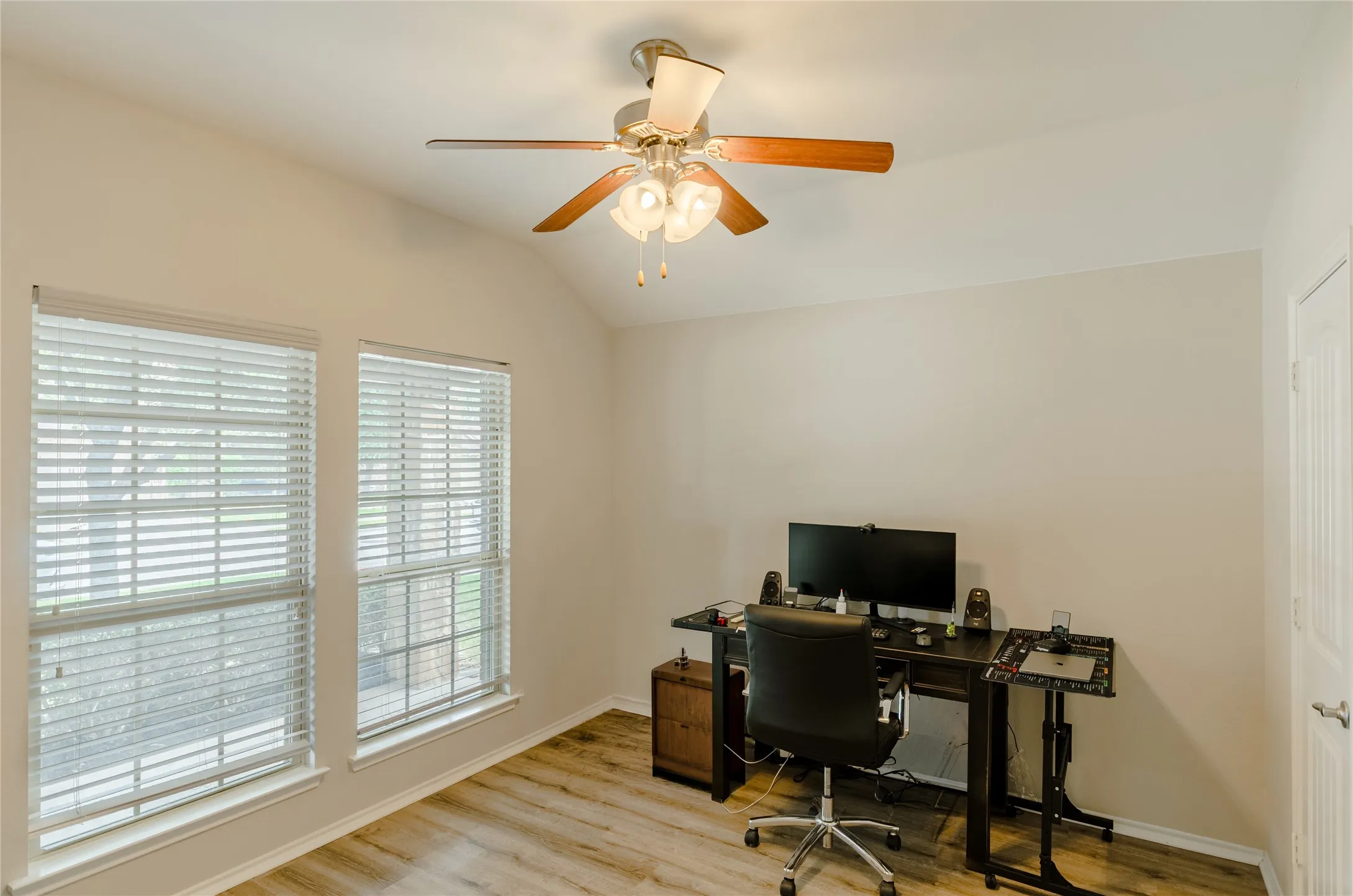 Vaulted ceiling room with two windows, wood-finish flooring, and a ceiling fan with integrated lighting