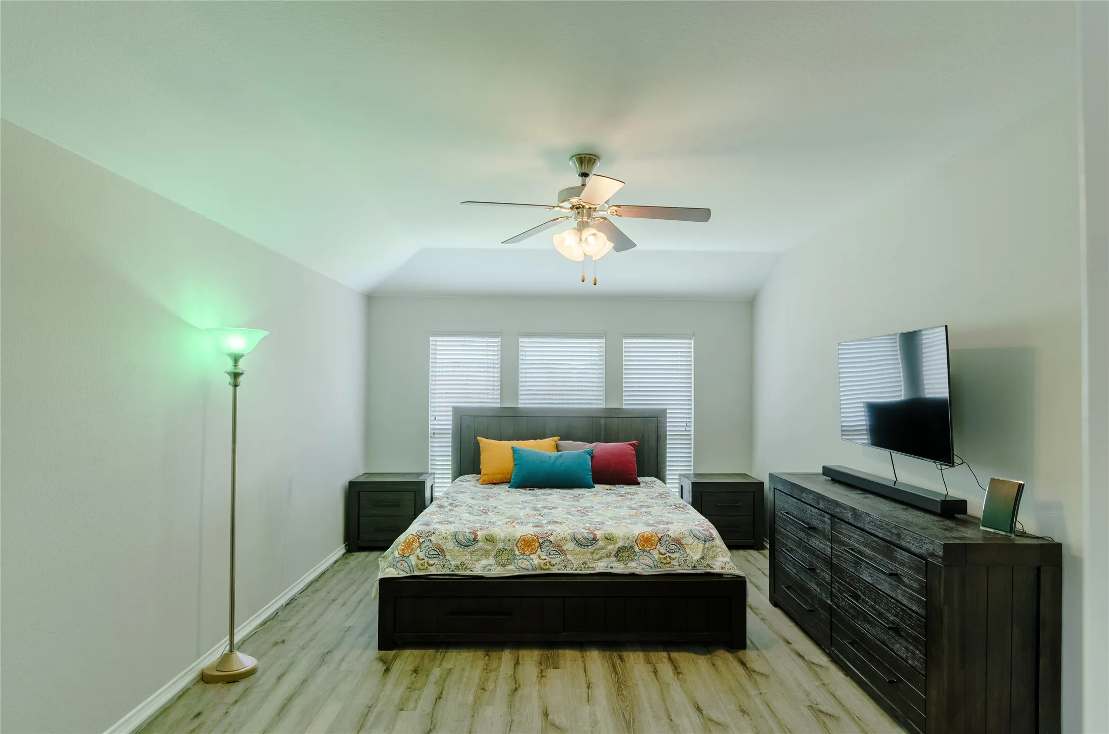 Spacious room featuring wood-finish flooring, a tray ceiling, and a ceiling fan with integrated lighting