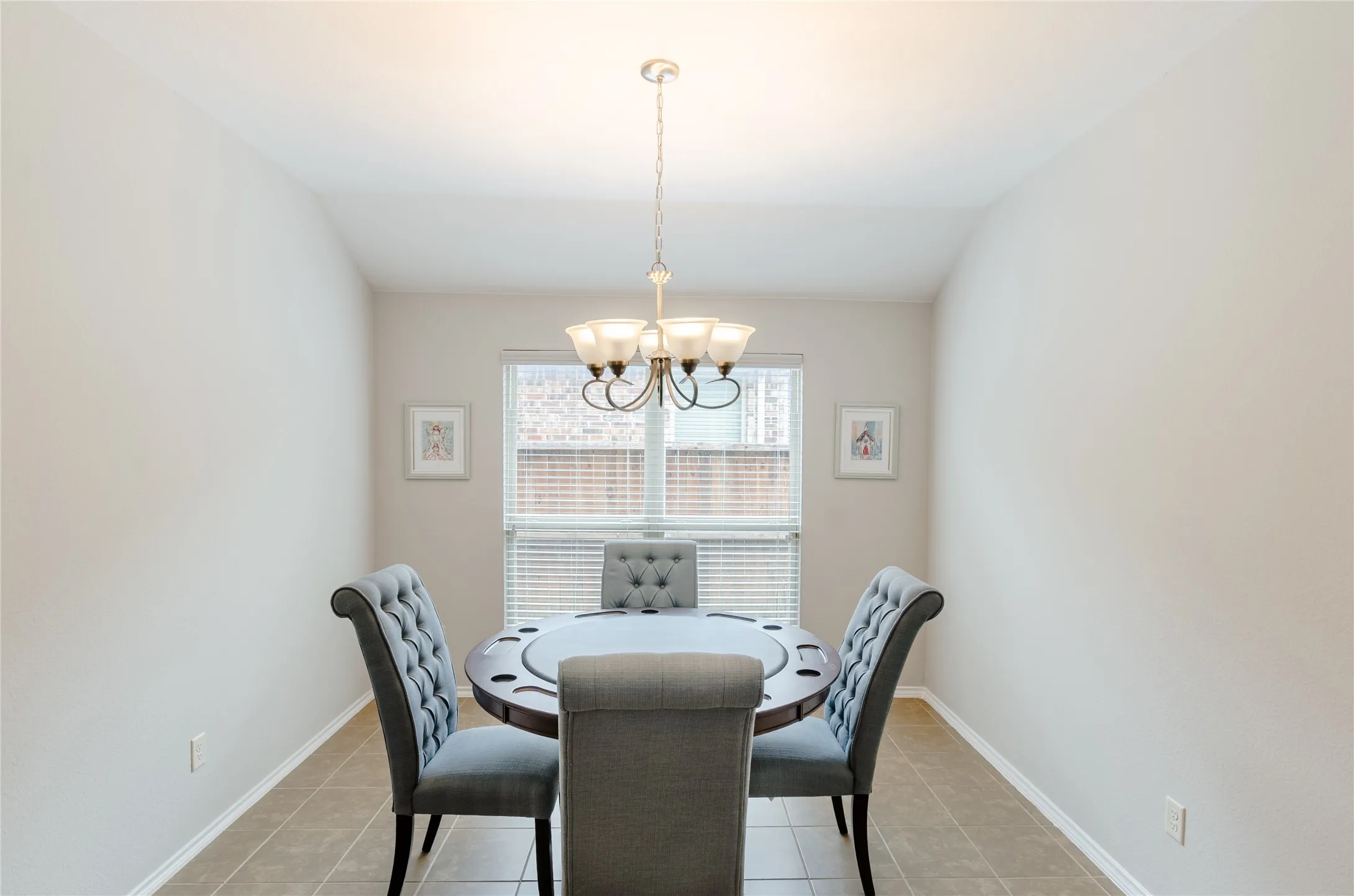 Dining space featuring a suspended chandelier with frosted glass shades, a window with horizontal blinds, and tiled flooring