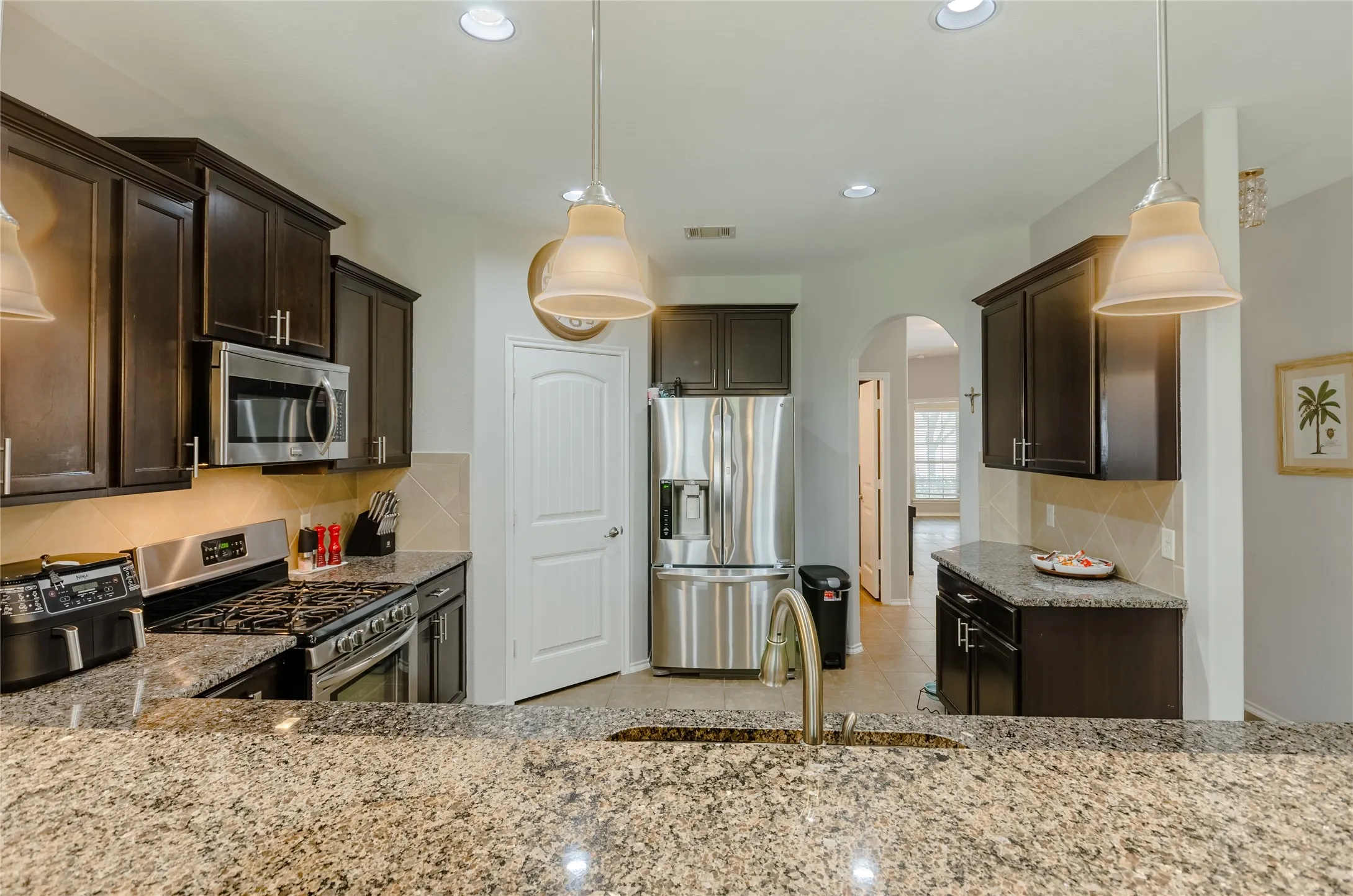 Kitchen featuring granite countertops, stainless steel appliances, dark wood cabinetry, recessed lighting, and pendant fixtures
