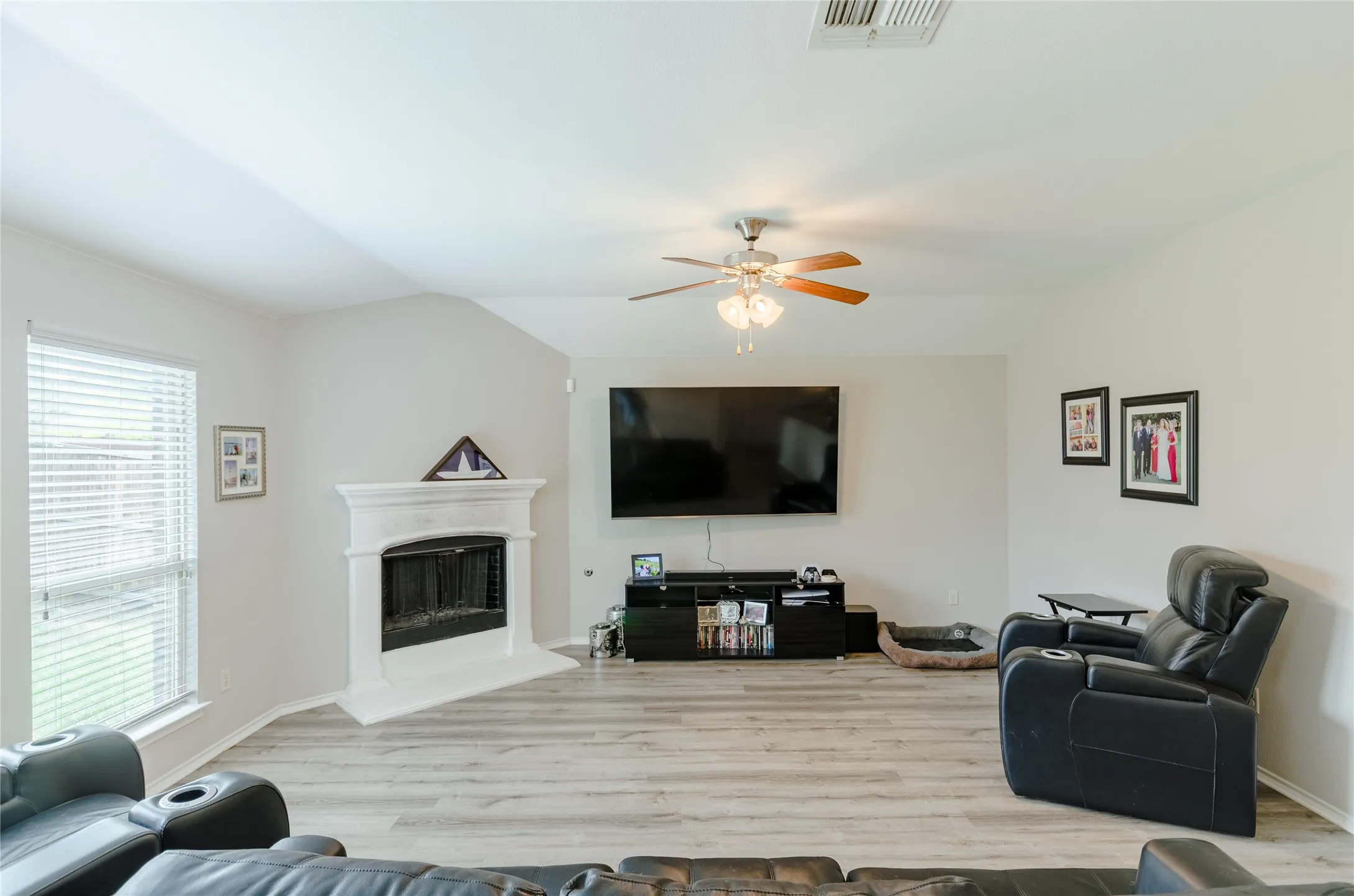 Living area featuring wood-finish flooring, a corner fireplace with a white mantel, and a ceiling fan with integrated lighting