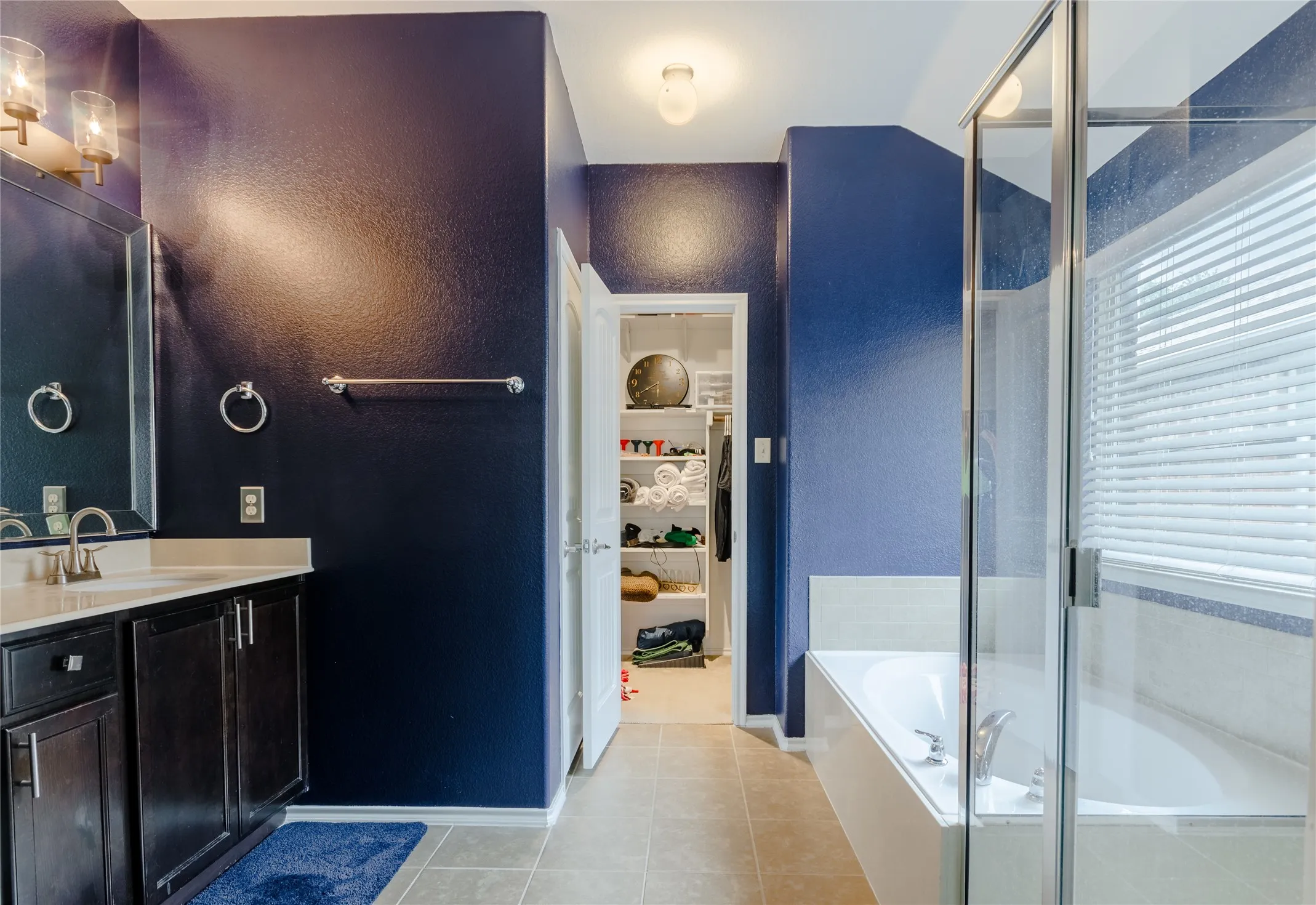 Bathroom featuring dark cabinetry, light countertop, a built-in tub, separate glass-enclosed shower, and a walk-in closet with shelving