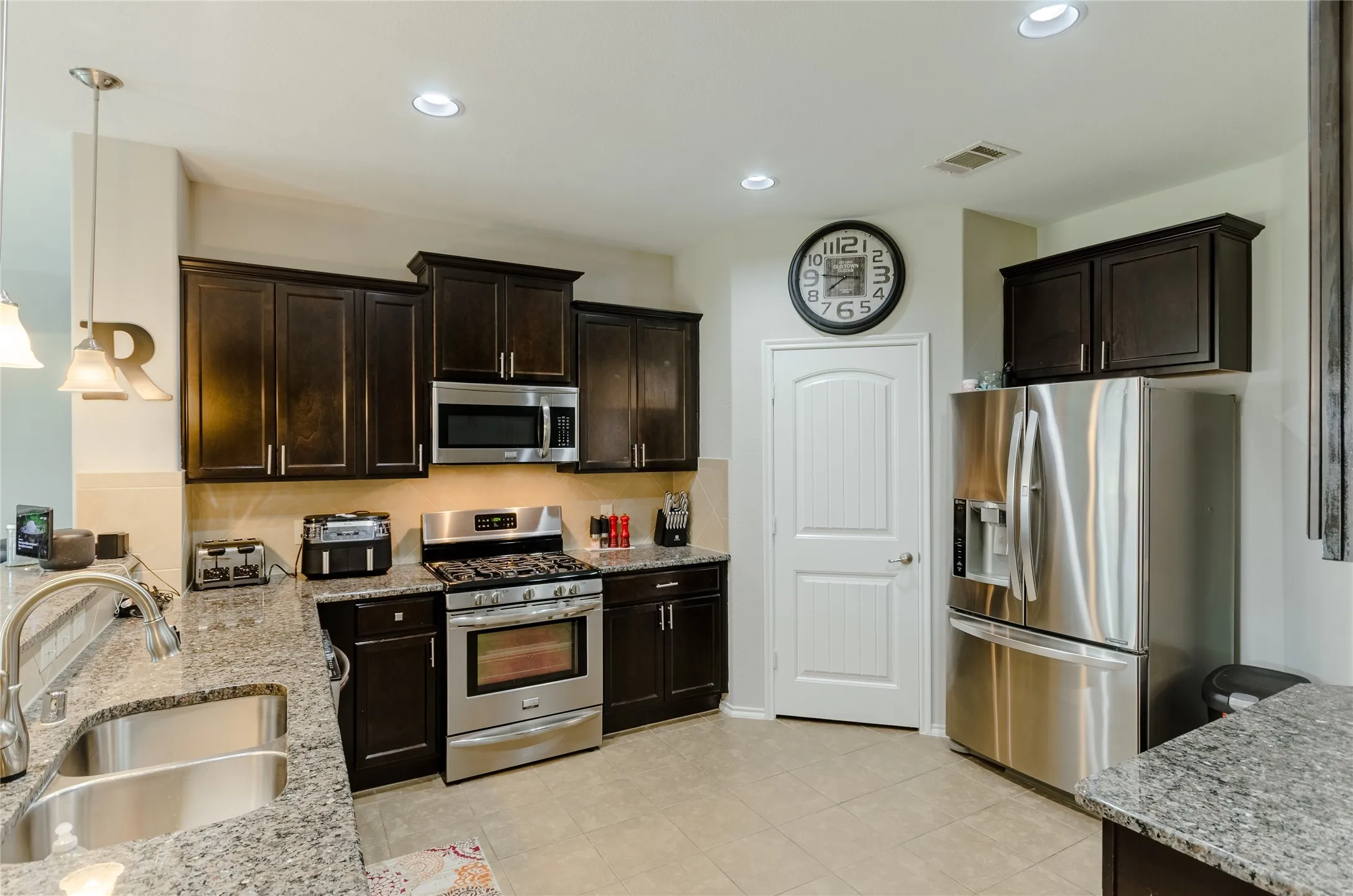 Kitchen featuring dark wood-finish cabinetry, stainless steel appliances including a gas range and French door refrigerator, and granite countertops