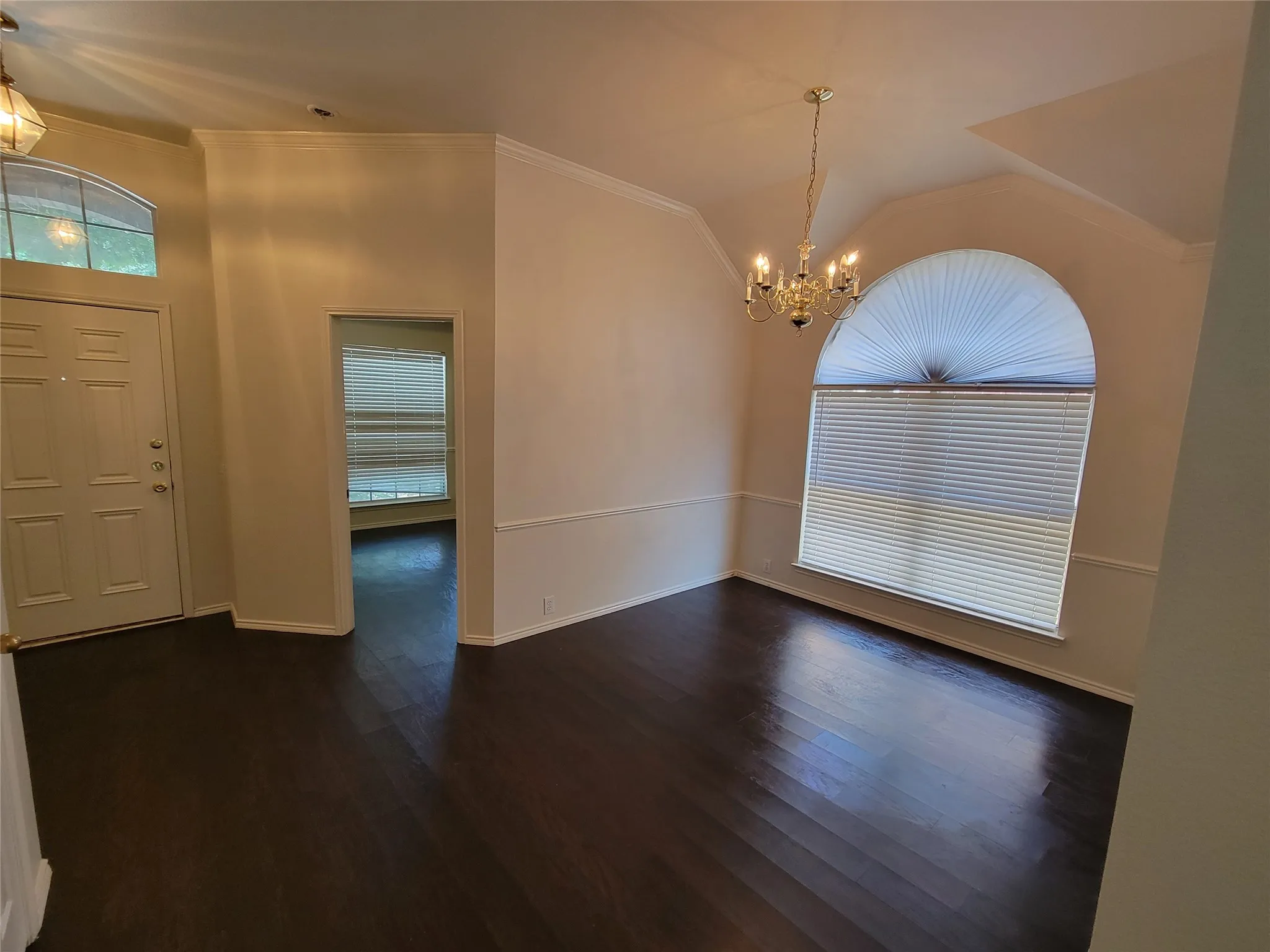 Entryway looking at dining room with chandelier, dark wood-style flooring, vaulted ceiling, and ornamental molding