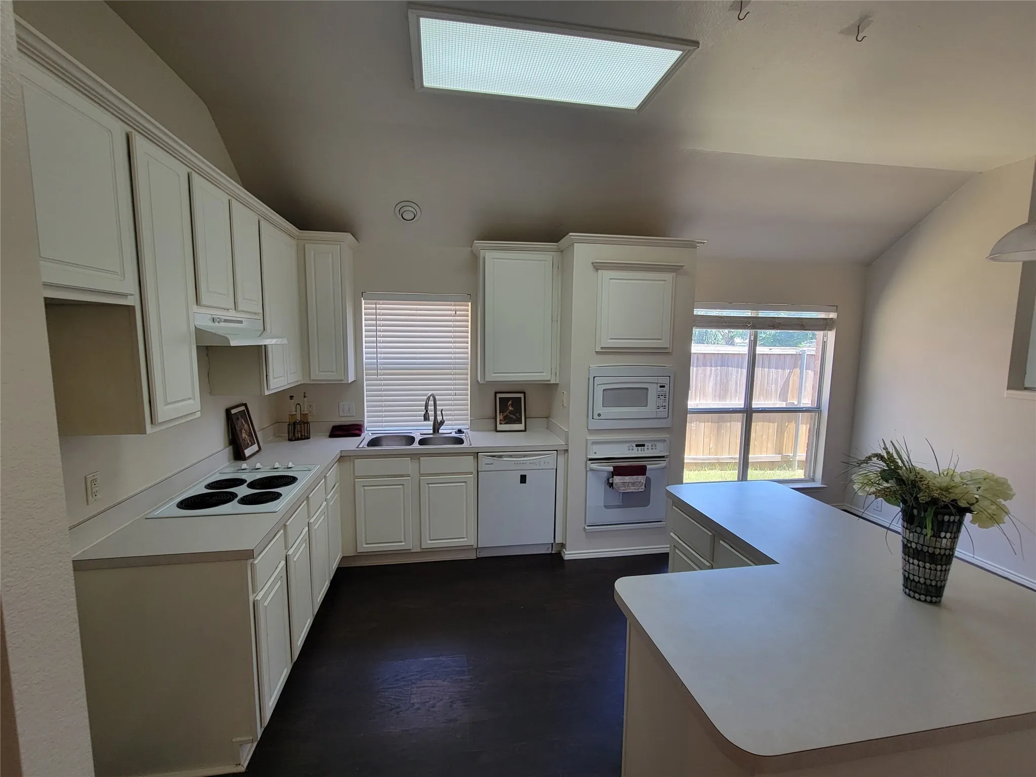 Kitchen with sink, white cabinetry, vaulted ceiling, and white appliances