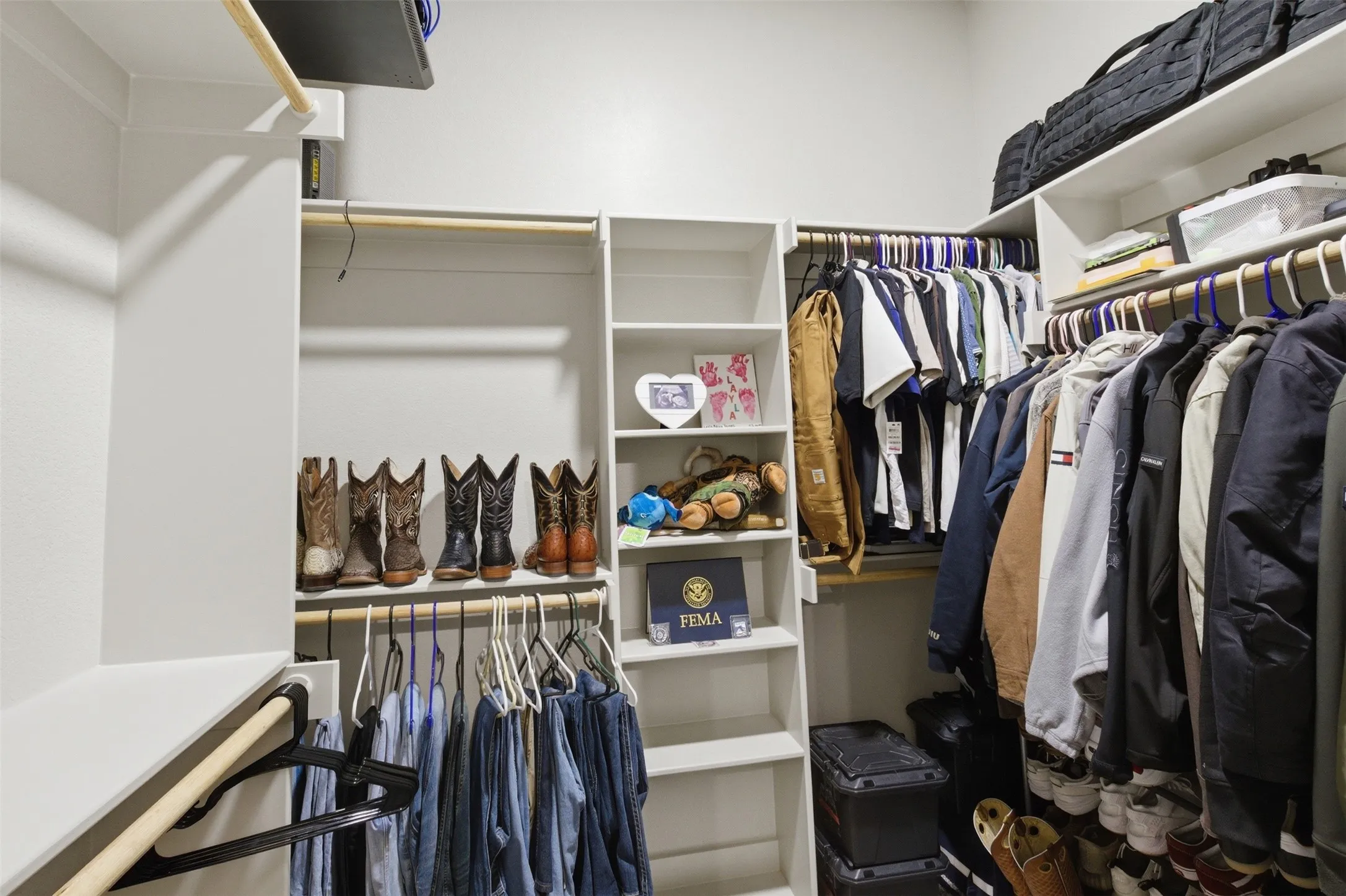 Walk-in closet featuring white built-in shelving, multiple hanging rods, and an upper storage shelf