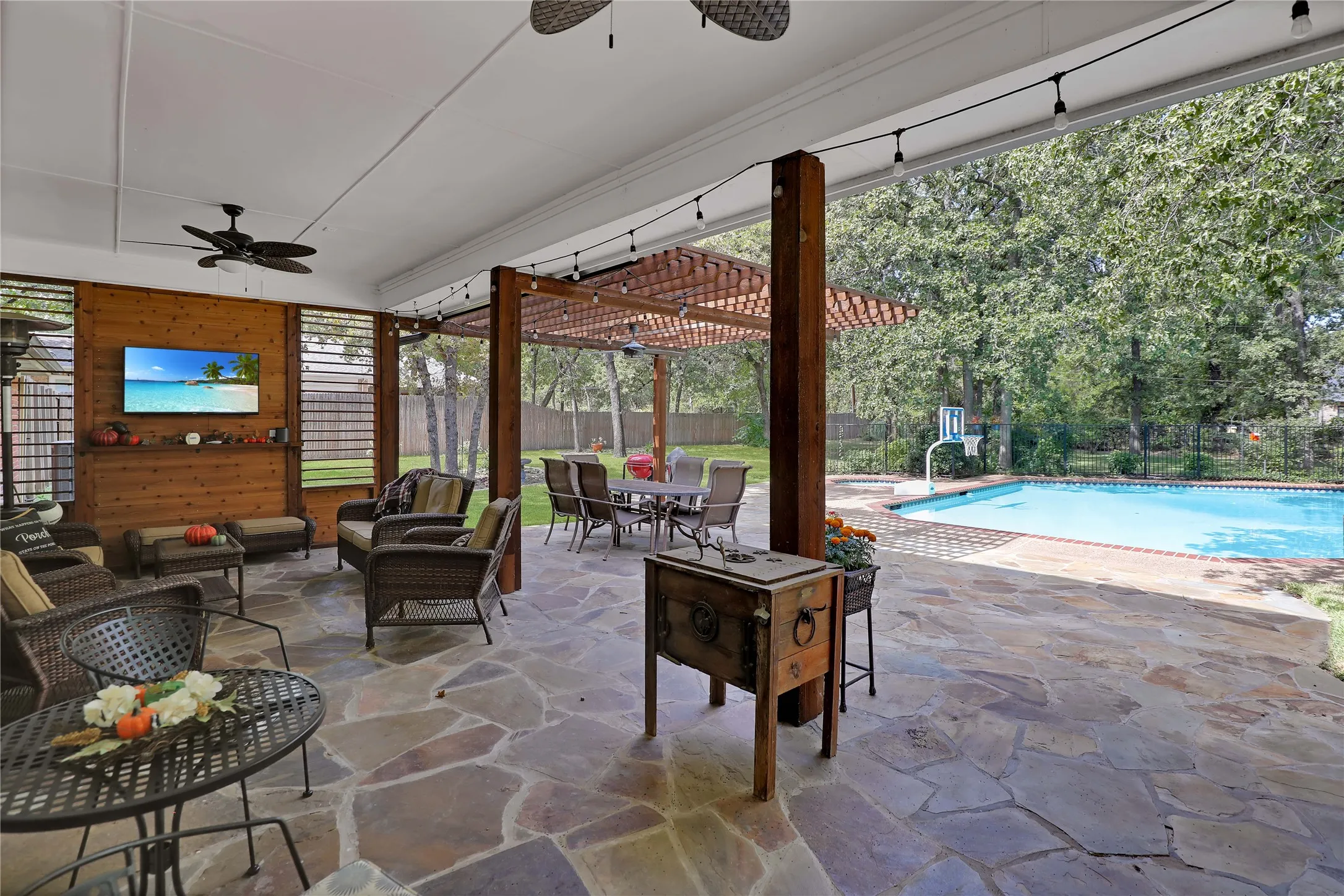 Covered natural stone patio with ceiling fans and outdoor living area with television