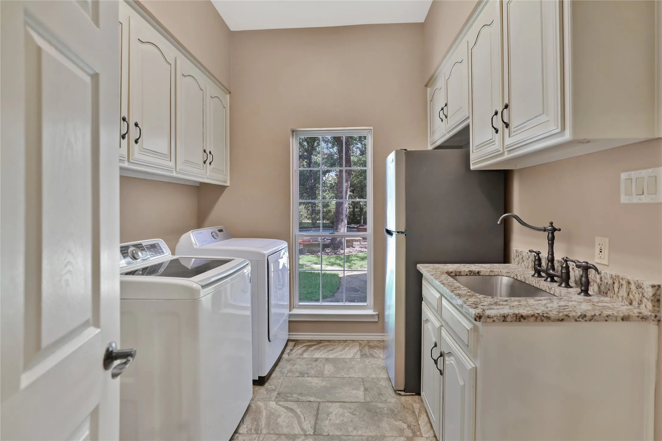 Large laundry room natural light, with sink, washer and dryer and extensive storage space in high cabinets