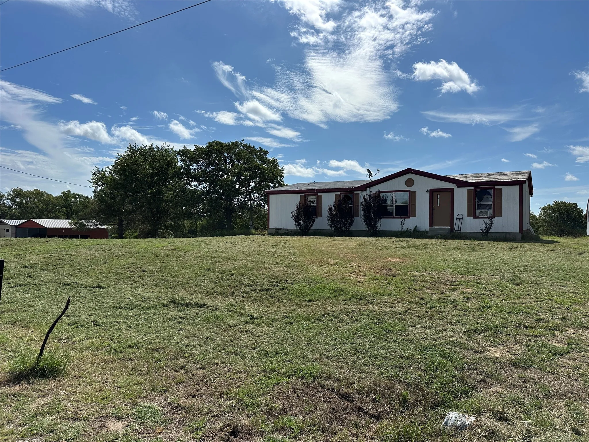 Spacious lot with a white single-story residence featuring a brown trim roof, multiple windows with brown shutters, and a front entry door