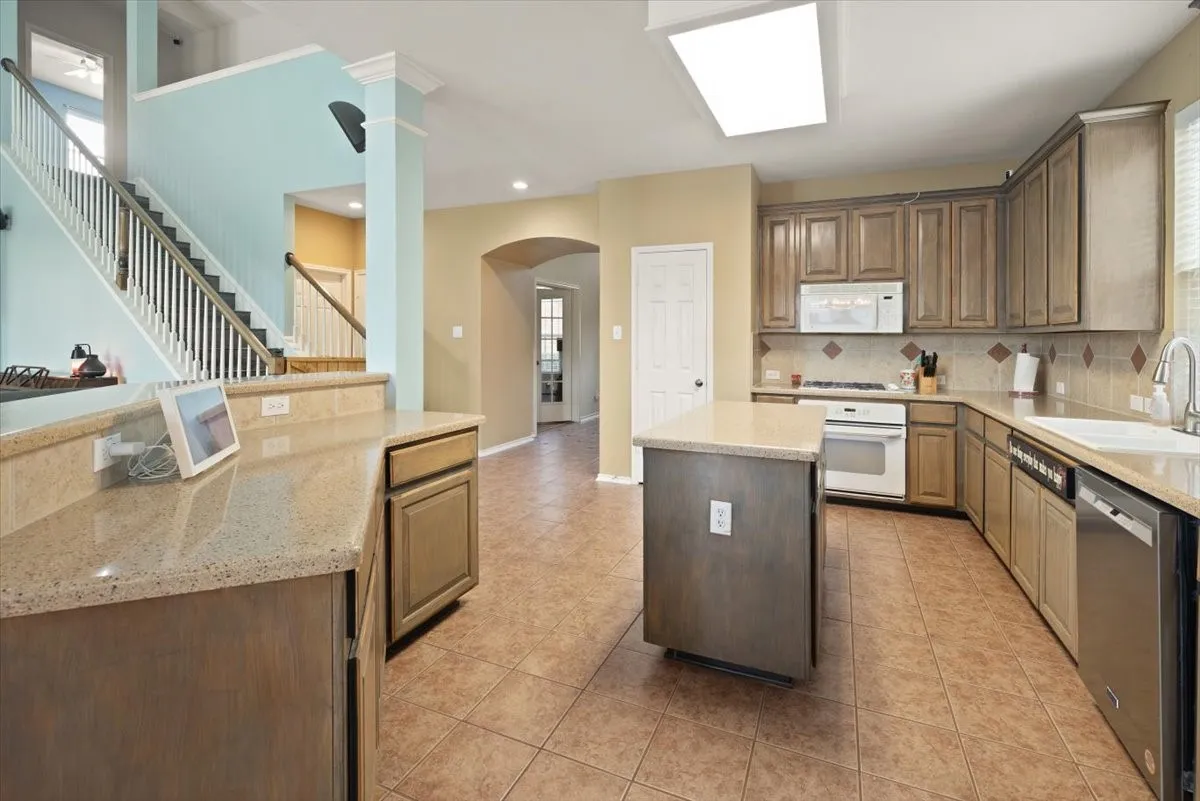 Kitchen featuring wood-finish cabinetry, light-toned countertops, a central island, and tile flooring