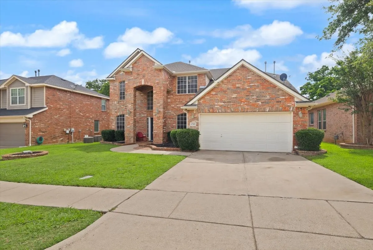 Two-story brick exterior with a prominent arched entry, an attached two-car garage, established front landscaping, a concrete driveway, and a front yard with a manicured lawn