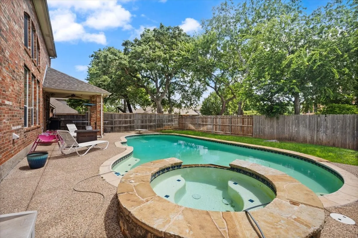 Expansive backyard featuring a freeform swimming pool, integrated spa with stone coping, and concrete patio