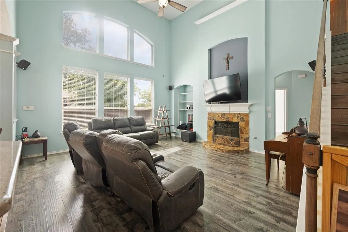 Two-story living area featuring wood-finish flooring, a stone-faced fireplace with a white mantel, and built-in shelving