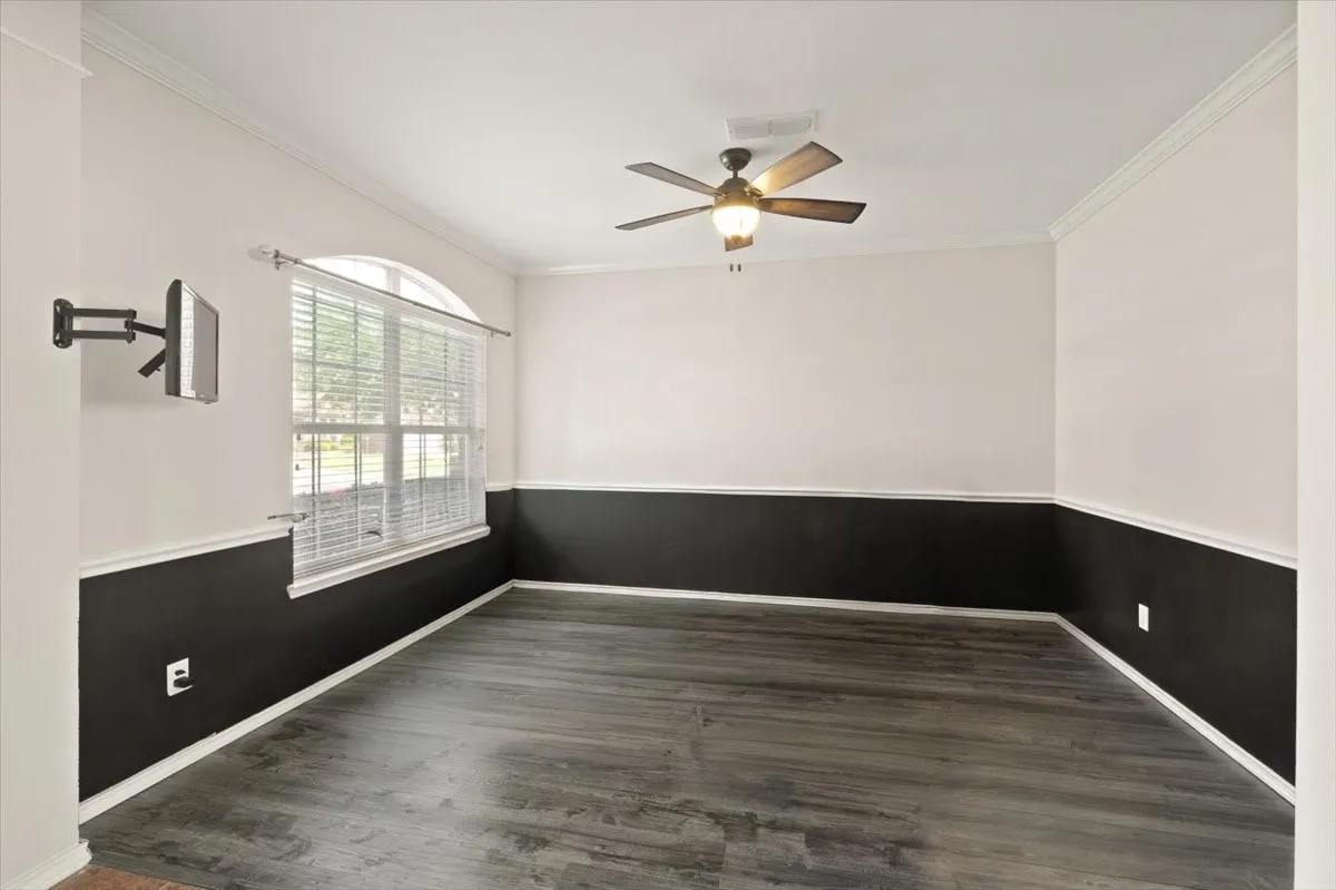 Spacious room featuring wood-finish flooring, two-tone wall treatment with wainscoting, crown molding, and an arched window with blinds