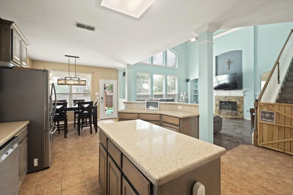 Open-concept kitchen and living area featuring a central island with a light-colored countertop, dark wood-finish cabinetry, and ceramic tile flooring