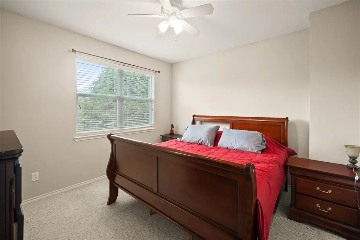Carpeted bedroom with a window featuring blinds, a ceiling fan with light fixture, and neutral wall tones