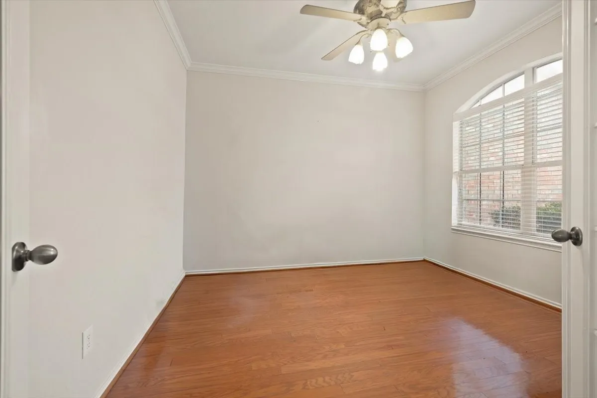 Room with wood-finish flooring, a ceiling fan with light fixture, and an arched window with blinds
