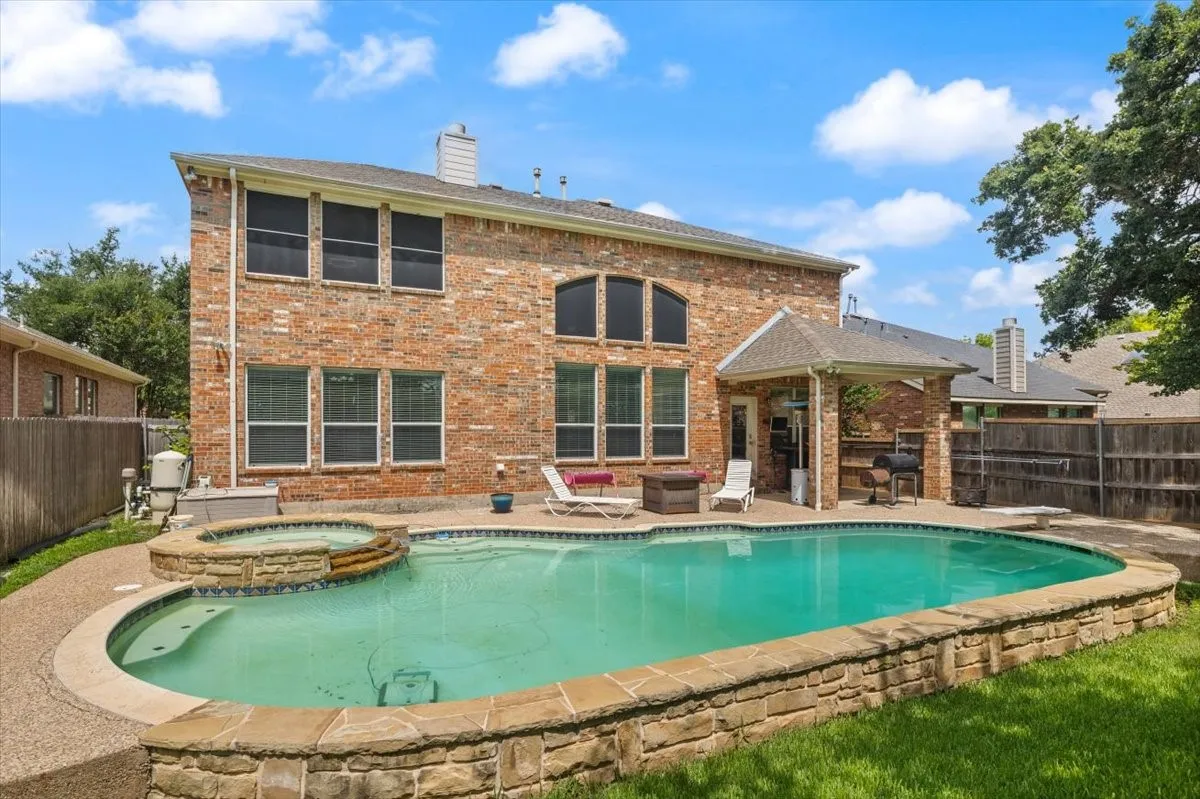 Expansive backyard featuring a large swimming pool with an integrated spa, stone coping, and a surrounding concrete patio