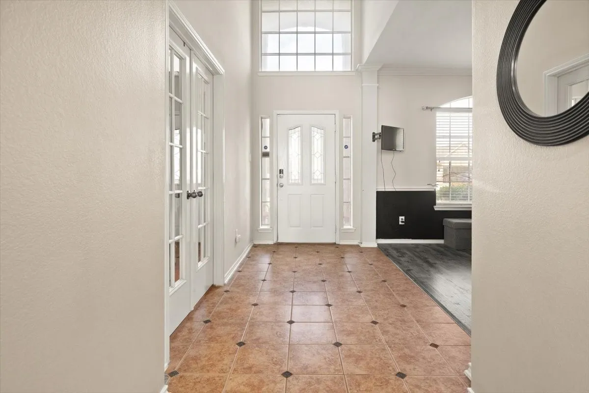 Foyer with high ceilings and transom windows, featuring French doors and a tile floor with accent squares