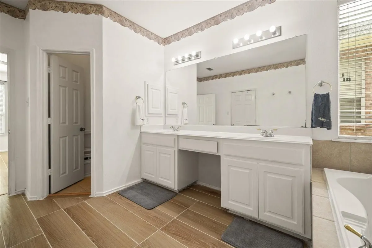 Bathroom featuring dual sinks with individual faucets, an expansive vanity mirror, and wood-finish tile flooring