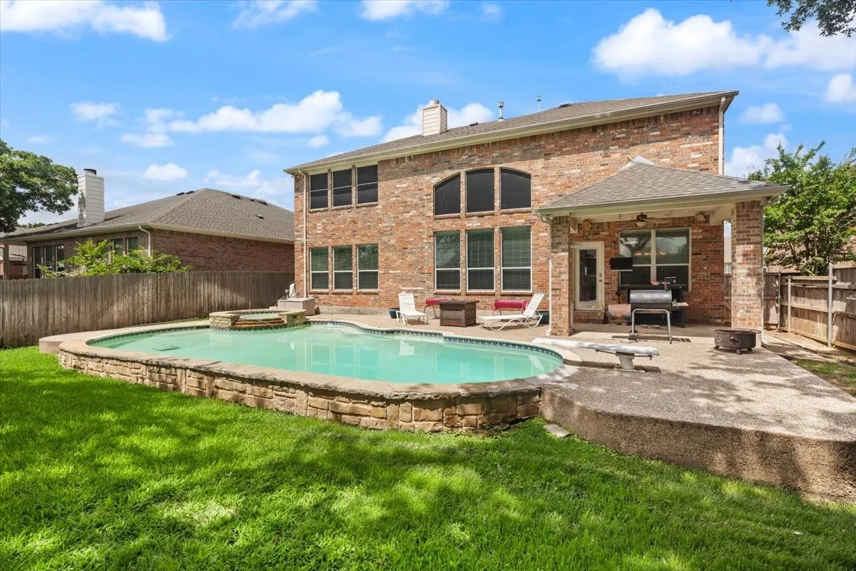Backyard featuring a stone-edged swimming pool with an integrated spa, expansive grass area, and a covered patio