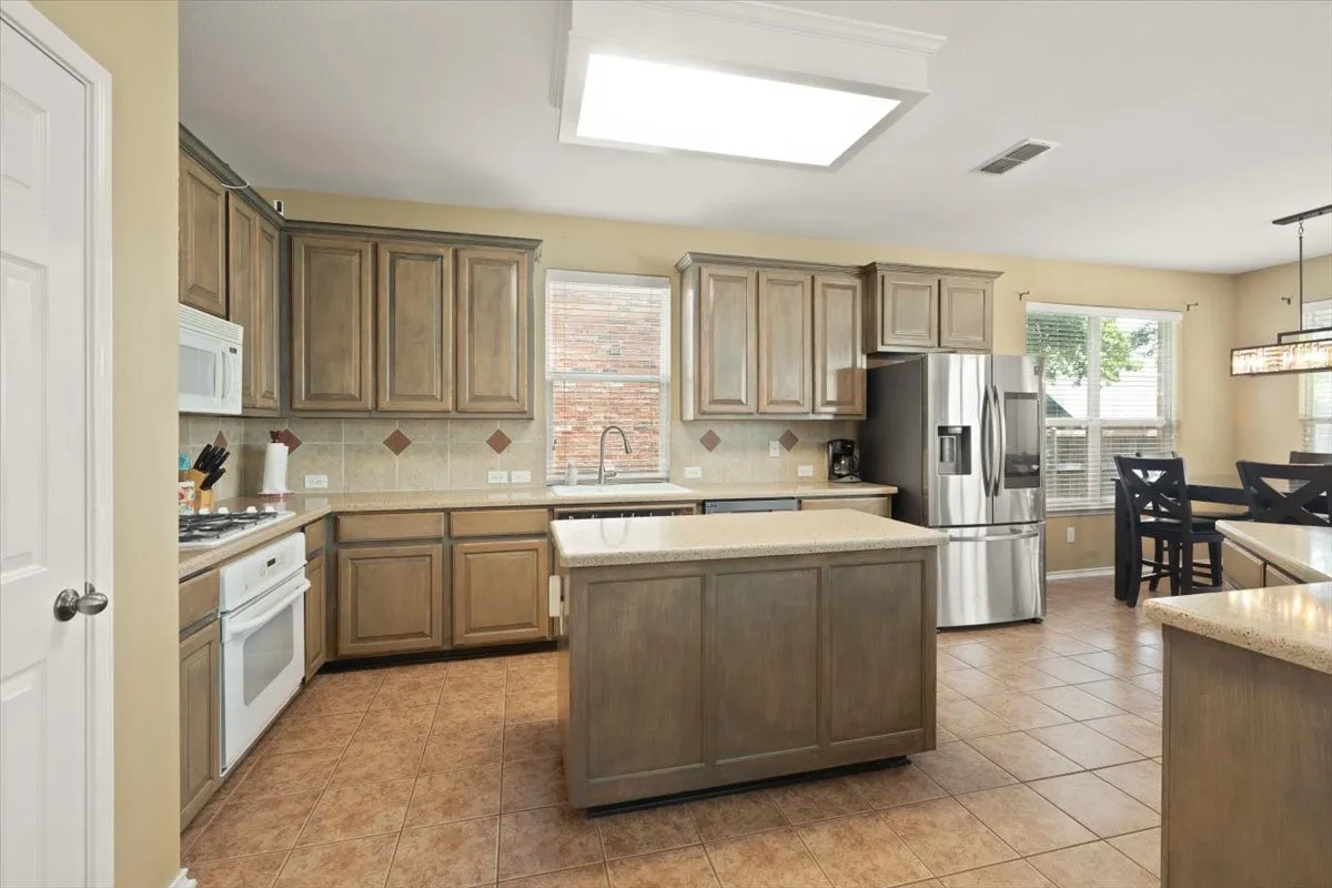 Kitchen featuring a central island, wood-finish cabinetry, tile flooring, stone-look countertops, and stainless steel appliances
