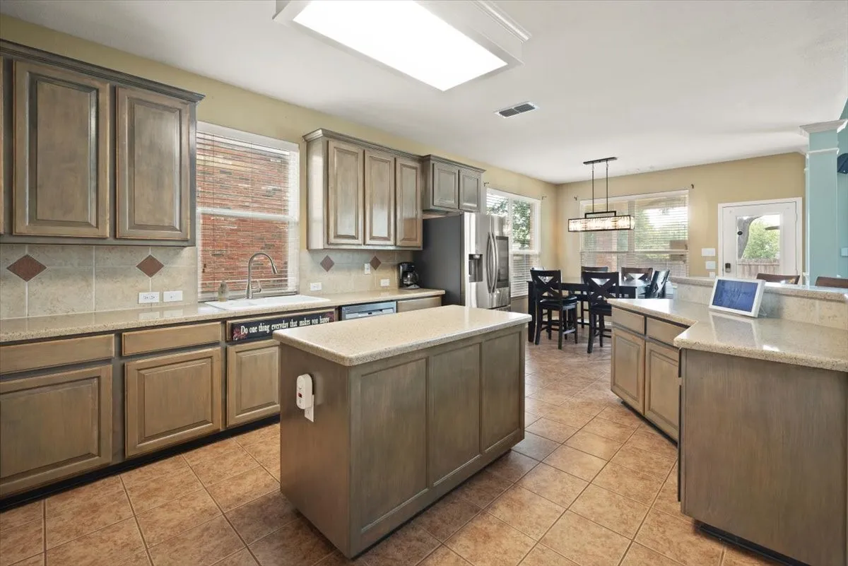 Kitchen featuring an expansive island, tiled flooring, wood-finish cabinetry, light-toned countertops, and a tiled backsplash with decorative accents