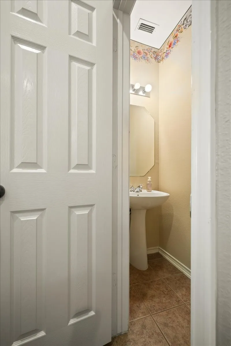 Powder room featuring a pedestal sink, ceramic tile flooring, an octagonal wall mirror, and a three-bulb vanity light fixture