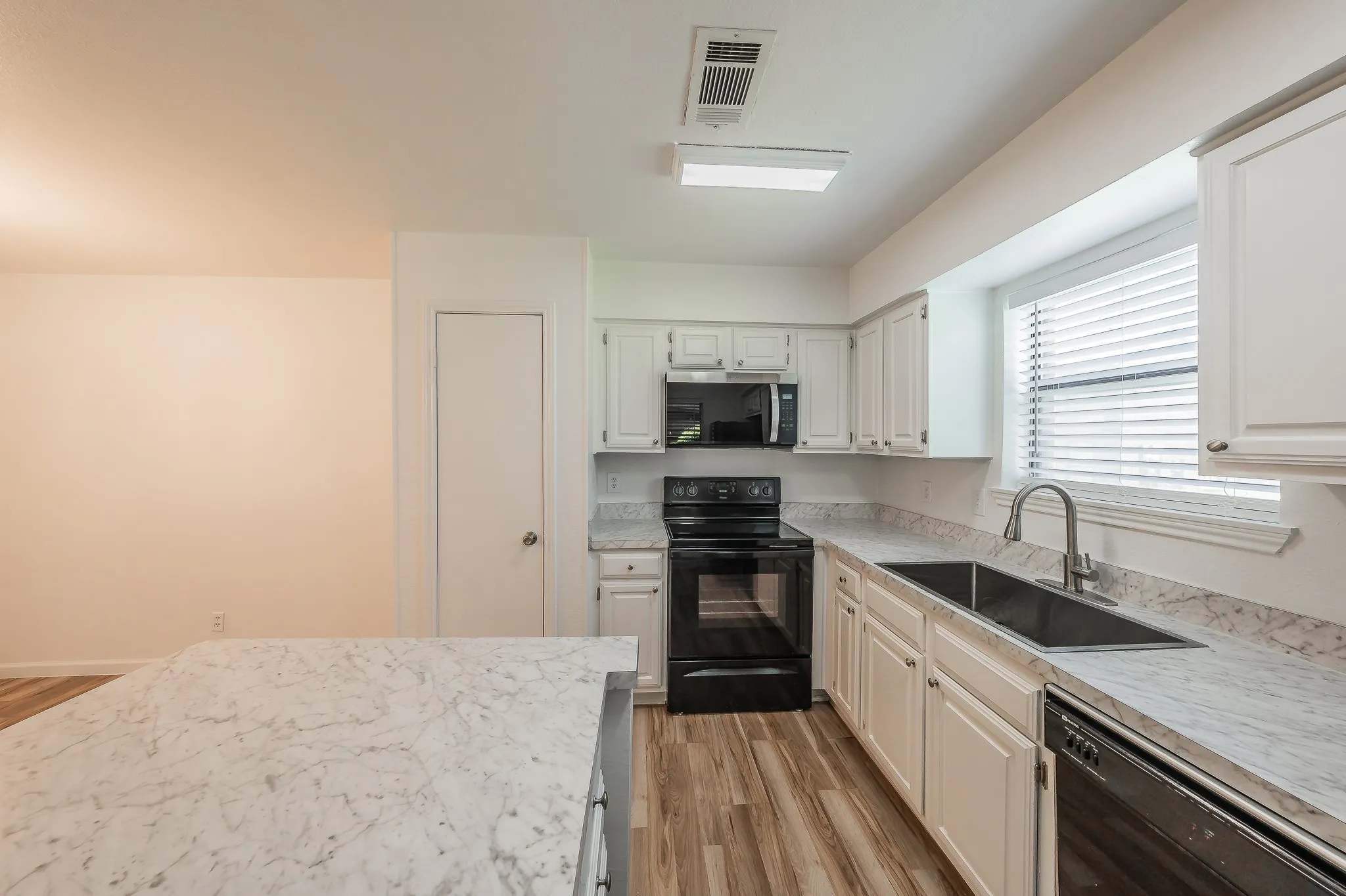 Kitchen featuring white cabinetry, black appliances, white patterned countertops, wood-finish flooring, and a double basin sink with a gooseneck faucet