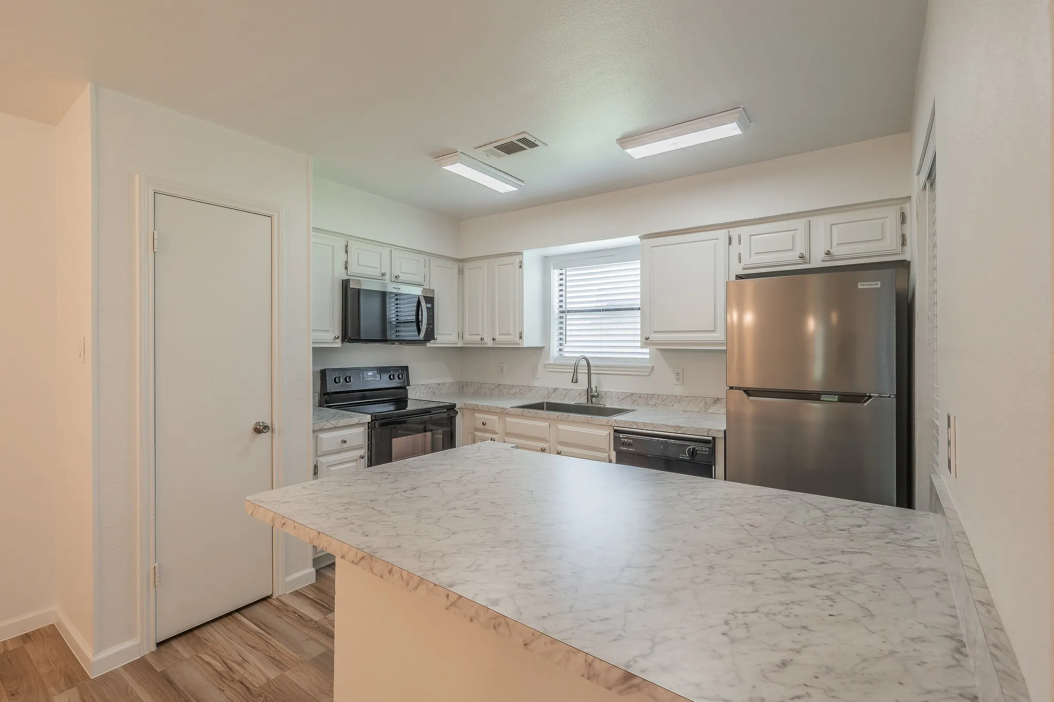 Kitchen featuring a peninsula island, white cabinetry, dark sink basin, stainless steel refrigerator, and wood-finish flooring