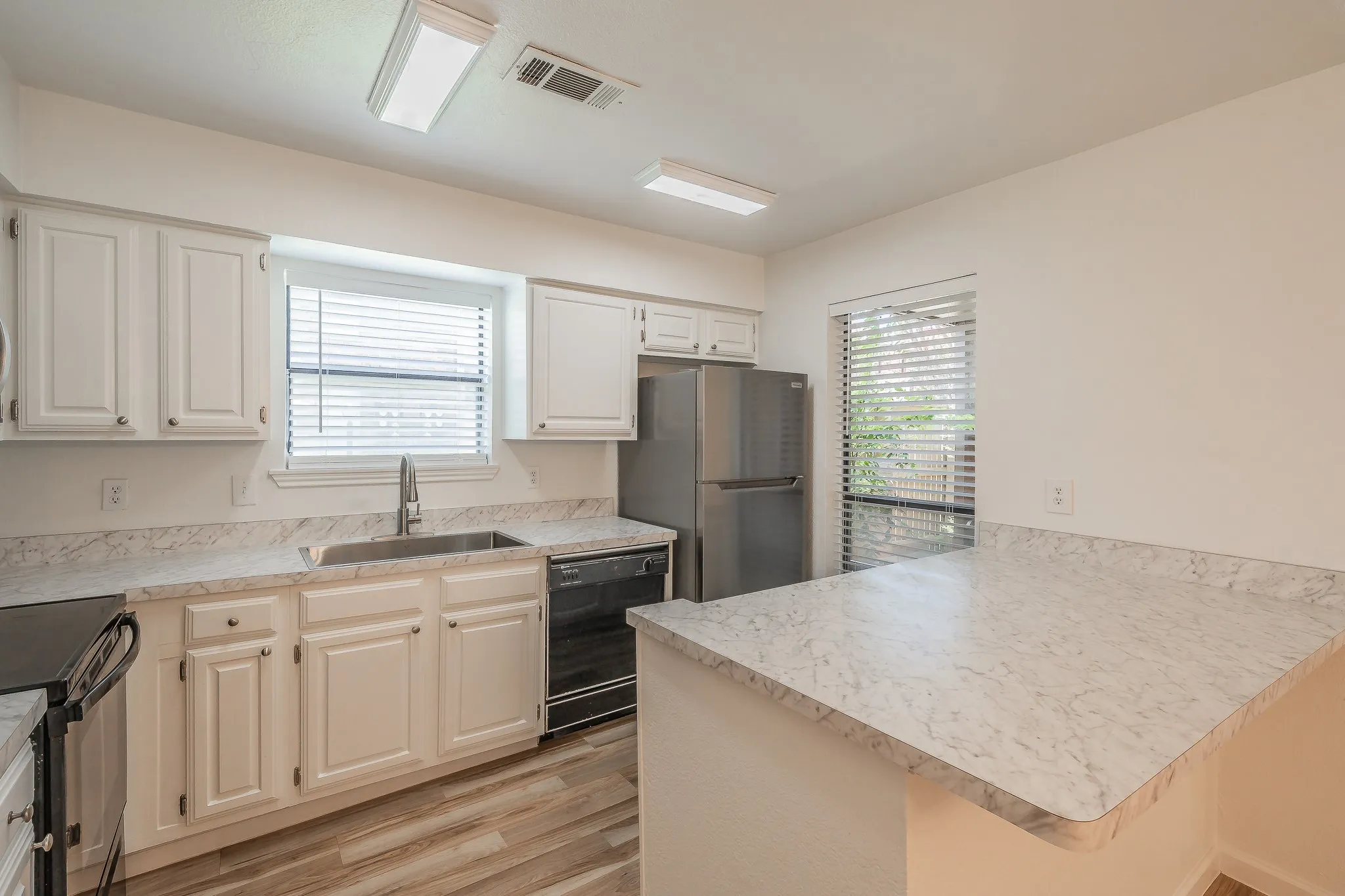 Kitchen featuring white cabinetry, wood-finish flooring, dishwasher, and white patterned countertops with an integrated sink