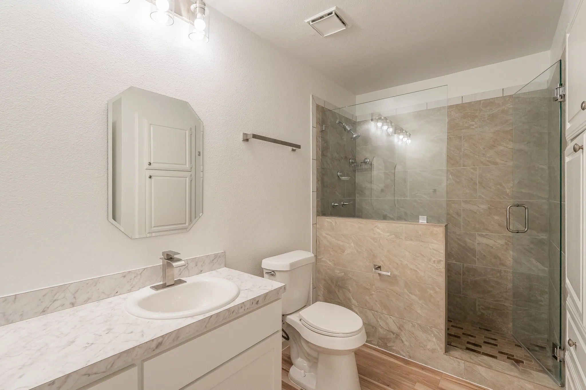 Bathroom featuring updated glass-enclosed shower with tile surround, double vanity with integrated sink and chrome faucet, new lighting and built-in storage cabinetry
