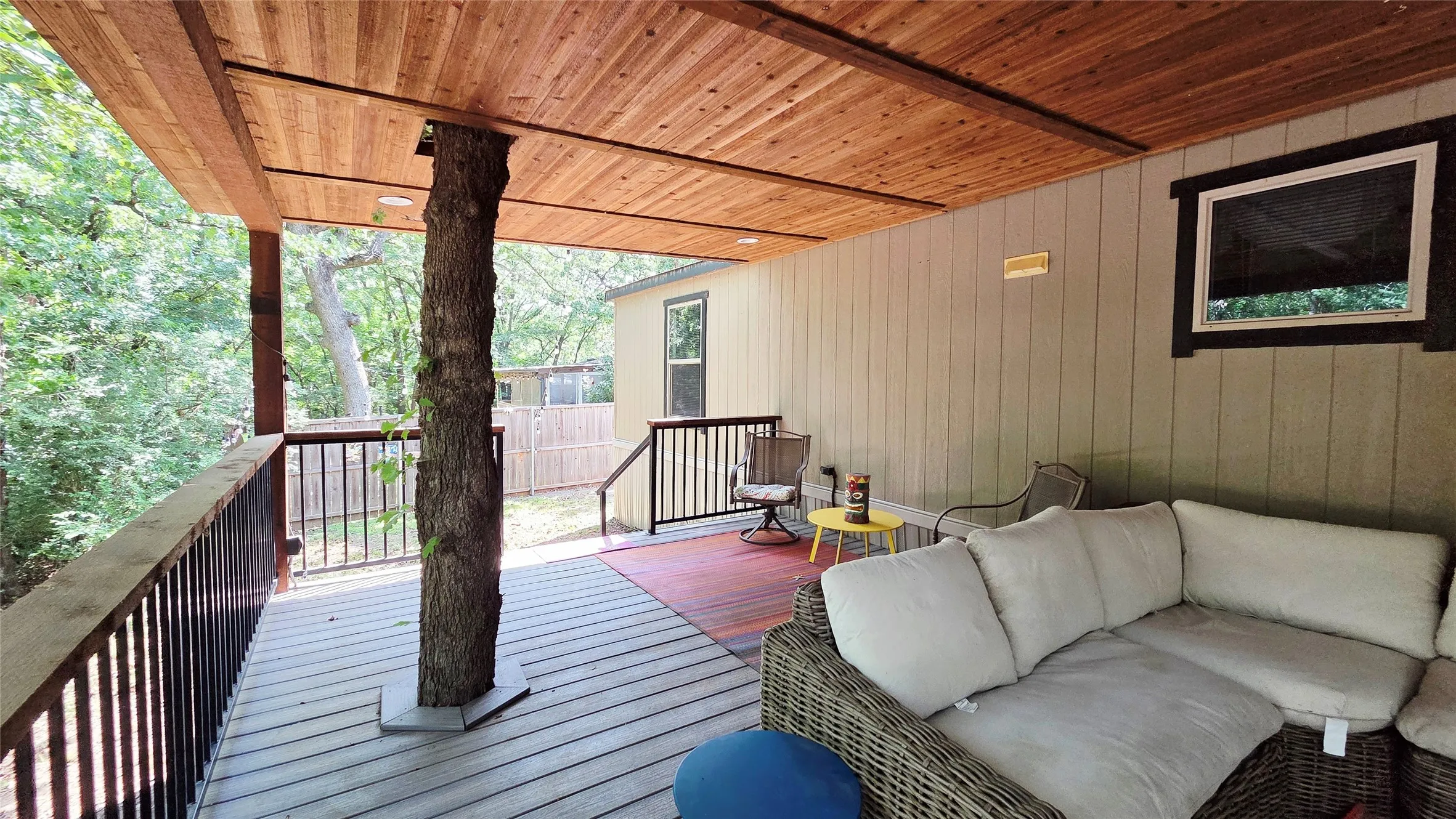Expansive covered deck featuring a natural tree support, wood-finish ceiling, composite decking, and black metal railings