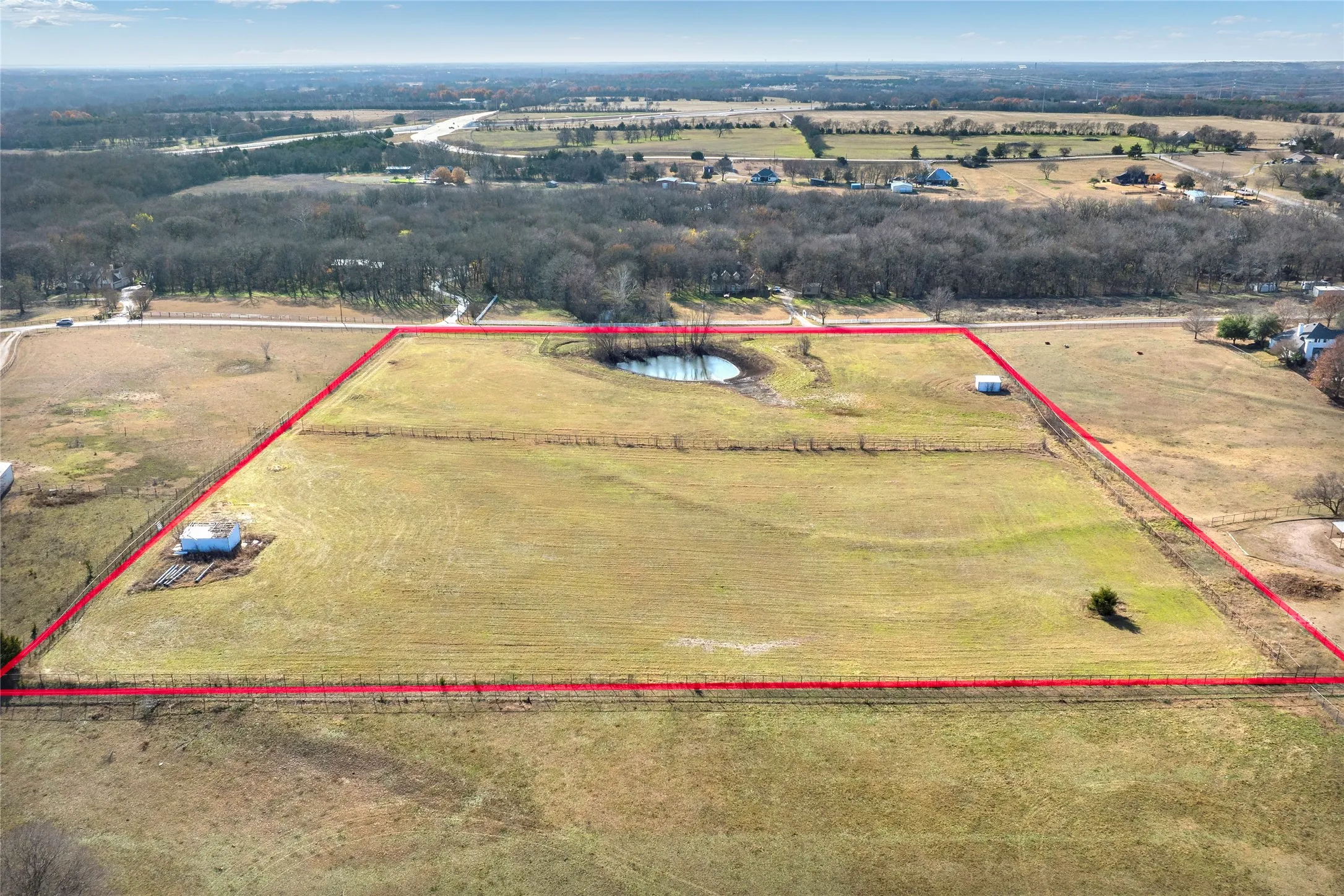 Expansive land parcel featuring a natural pond, perimeter fencing, existing outbuildings, and a single tree
