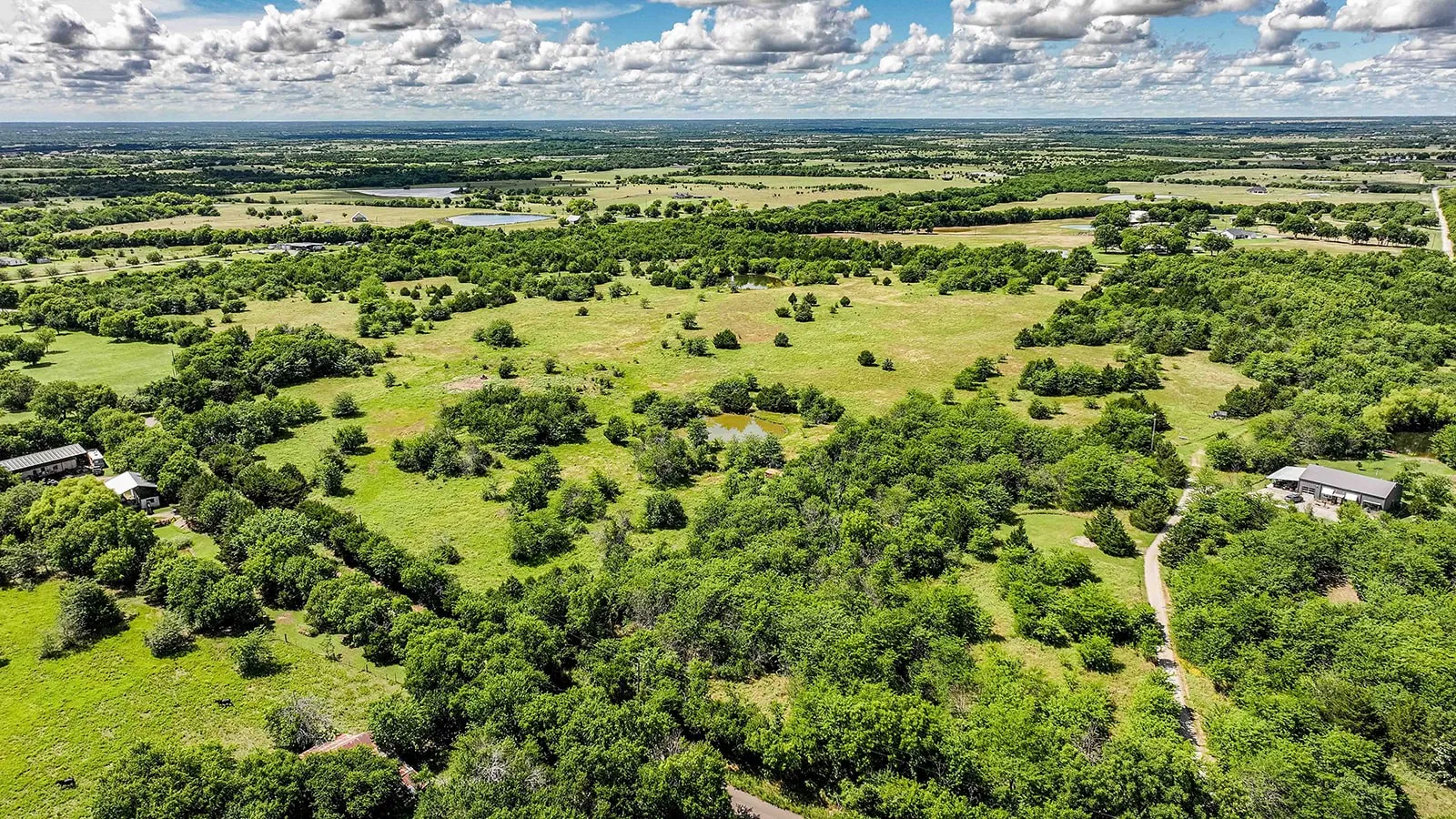 Expansive rural landscape featuring scattered mature trees, open pastures, and a pond