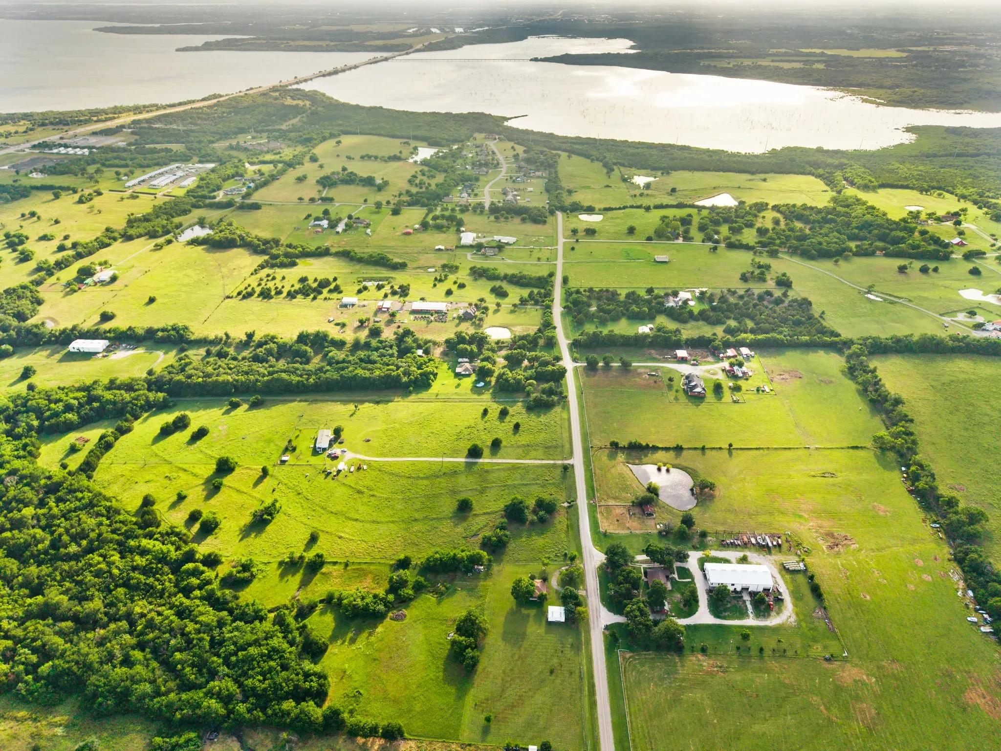 Expansive aerial landscape featuring a large body of water, a bridge crossing the water, and verdant green fields