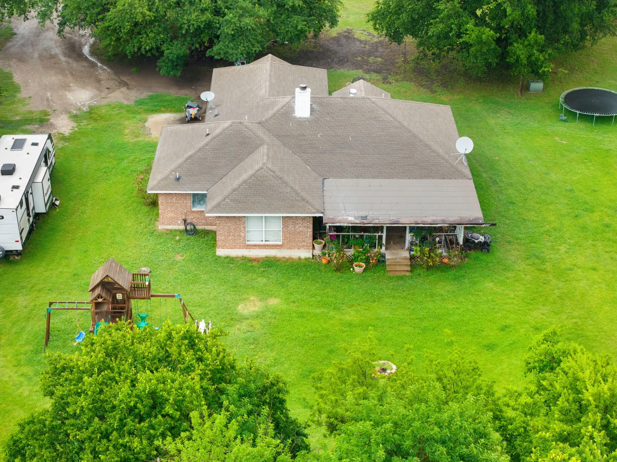 Brick exterior residence with a shingle roof, featuring a covered porch, a chimney, and expansive green grounds