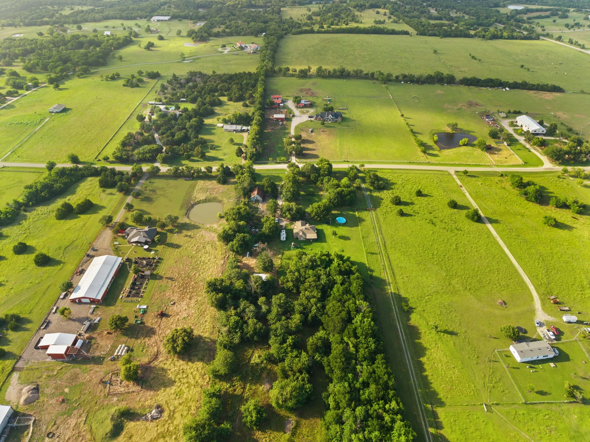 Expansive green landscape featuring multiple structures, open fields, mature trees, and visible roads